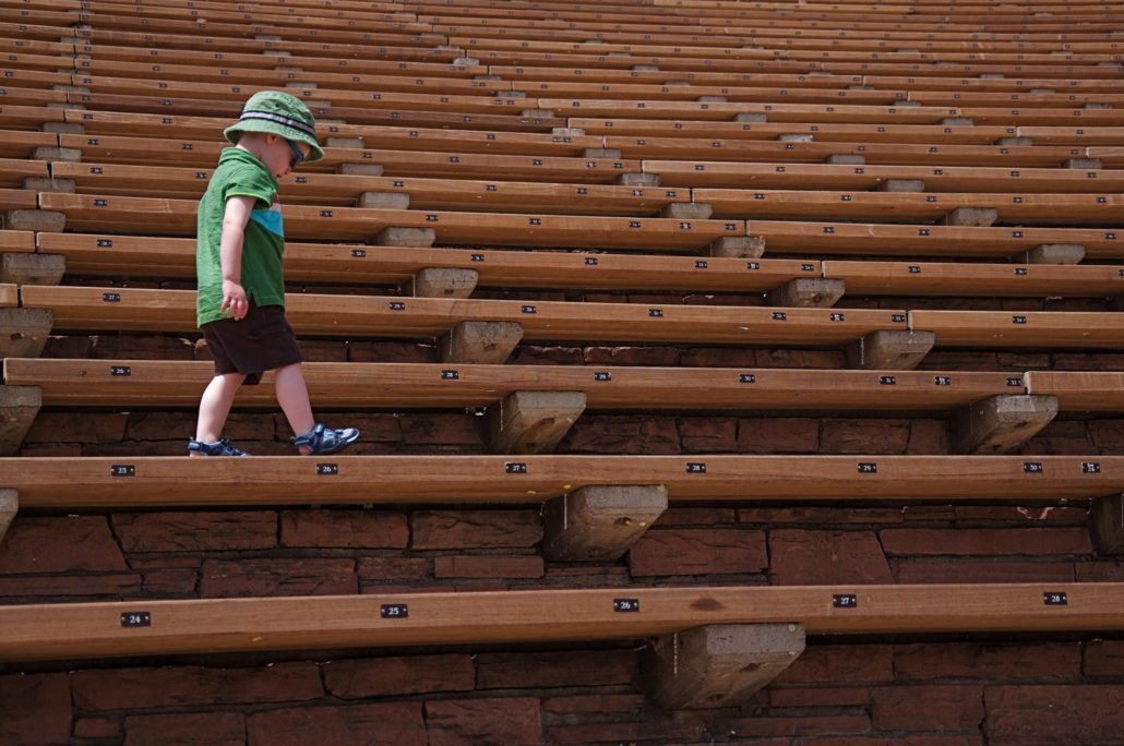little boy walks along the seats at Red Rocks Amphitheater in Morrison, Colorado.